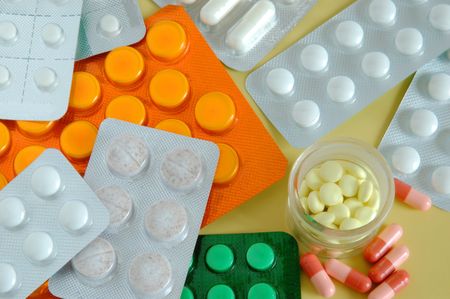 Lots of pills in their containers on yellow background