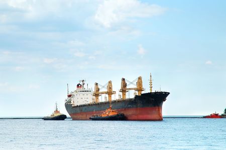 Container ship coming into port with tugboats