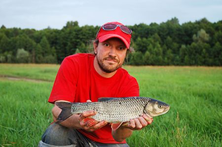 Fisherman holding a rudd fish on the shoreline of a river