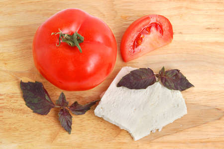 Tomatoe with white cheese slices and basil on cutting board backgroundの写真素材