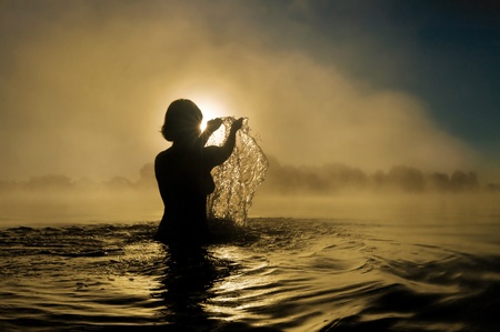 Silhouette of a young girl with raised arms in the waterの写真素材