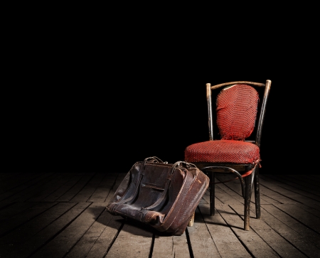 Old red chair and well-traveled vintage suitcase on wooden floorの写真素材