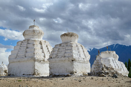 White buddhist chortens (stupas) and Himalayas mountains on the background in valley near Leh, Ladakh, Indiaの写真素材