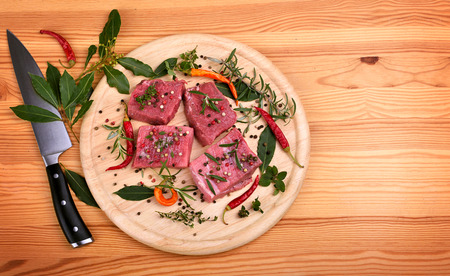 Fresh raw beef meat with color peppercorn and rosemary on a round cutting board