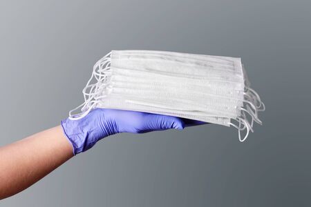 Hand in blue medical glove give a stack of surgical masks for protect corona virus isolated on gray