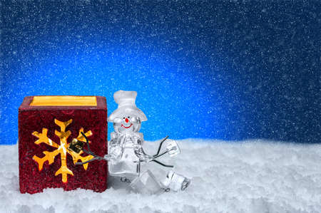 Snowman in hat and a candle in a candlestick with a snowflake on a blue background. Snowing and snowdriftsの写真素材