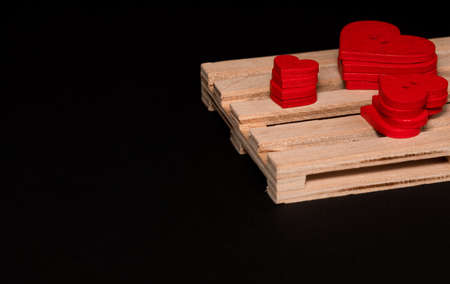Red buttons in the form of a heart lie on a wooden pallet against a black backgroundの写真素材