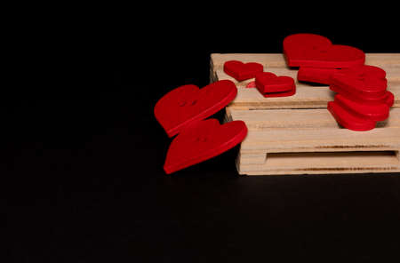 Many red buttons in the form of a heart lie on a wooden pallet against a black backgroundの写真素材