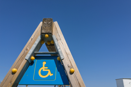 disabled sign and simbol on wooden swing pole, playground with clear blue sky. pole, playground with clear blue sky.の写真素材