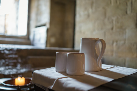 Selective focus on white ceramic tea pot and tea cup with light from window and candle in the morning, warm vintage atmosphere.の写真素材