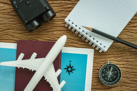 Travel planning concept with airplane, passport, compass, binoculars, pencil and paper note on wood table.の写真素材