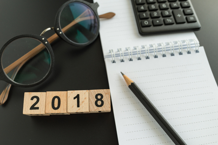 financial target concept as selective focus on number 2018 wooden block with glasses, calculator, pencil, notebook.の写真素材