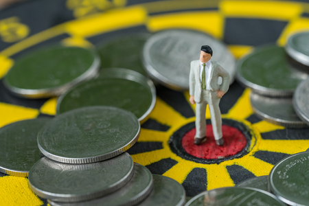 financial business concept as miniature business man standing at the center of dartboard with coins around.の写真素材