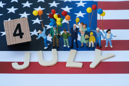 miniature people, happy american family holding balloon and wooden block and alphabet as 4 July with United State national flag in the background as celebrating the Independence day.の写真素材