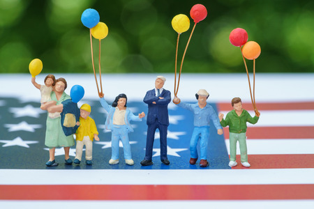miniature figure, happy american family holding balloon with United State national flag in green bokeh background as celebrating the Independence day.の写真素材