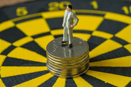 miniature business concept as figure of businessman standing on stack of coins at the center of...