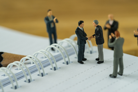 Miniature people businessmen handshaking and others clapping on notebook as business agreement concept.の写真素材