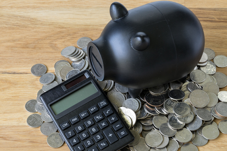 black piggy bank with calculator and coins on wooden table as saving or financial concept.の写真素材