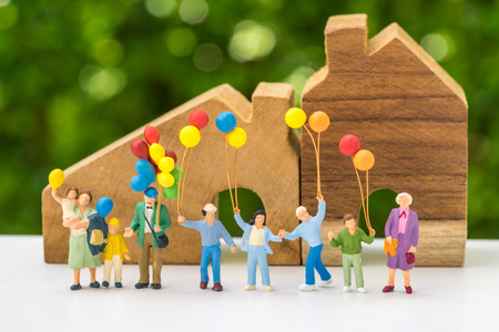 Miniature people with happy family holding balloons with wooden house as property or mortgage concept.の写真素材