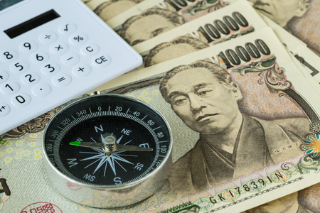 Compass and calculator on pile of japanese yen banknotes as financial safe haven or tax concept.の写真素材