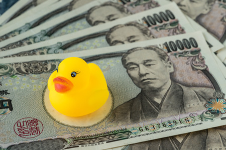 Selective focus on yellow duck doll on pile of japanese yen banknotes as financial crisis or tax concept.の写真素材