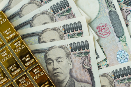 gold bullion ingot and pile of japanese yen banknotes as financial safe haven or investment concept.の写真素材