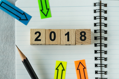 selective focus on wooden cube block 2018 with arrows pad on note paper as new year 2018 aim or goals concept.の写真素材