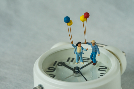 miniature happy family holding balloons standing on white alarm clock as happy people on time deadline concept.の写真素材