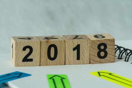 selective focus on wooden cube block with number 2018 with arrows pad on note paper as new year 2018...