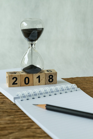 new year 2018 goals, target or checklist concept as number 2018 wooden cube block with sandglass and white paper note with pencil on wooden table.の写真素材
