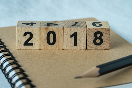 selective focus on wooden cube block with number 2018 on brown notebook and pencil as new year 2018 aim or goals concept.の写真素材
