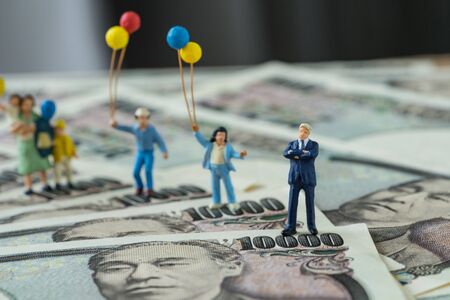 Miniature figure happy leader with his family holding balloons standing on japan yen banknotes as financial business leader concept.の写真素材