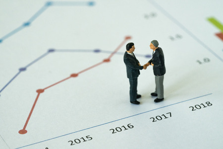 Miniature people with small figure businessmen handshaking on printed analysis growth chart graph as business agreement for success concept.の写真素材