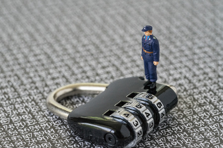Computer security or hacker protection concept, with miniature figure security guard standing on combination lock pad with the background of computer numbers secret code.の写真素材