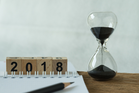 New year 2018 goals, target or checklist concept as sandglass and white paper note with pencil and number 2018 wooden cube block.の写真素材
