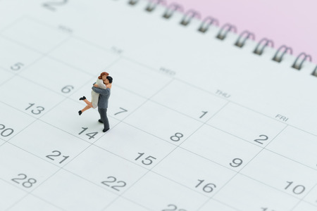 Valentines day reminder with lovely miniature couple standing on 14 Feb calendar on pink background.の写真素材
