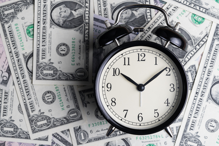 Black alarm clock on US dollar banknotes as time for money awareness concept.