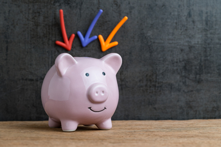 Business or finance saving concept by pink piggy bank on wooden table having colorful arrow pointing on it sticked on dark black background.の写真素材