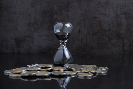 Long term investment or financial time counting down concept, sandglass / hourglass with coins on black table and black cement loft background.の写真素材