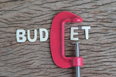 Finance, economy and business squeezing idea, wooden alphabet of the word BUDGET using red clamp as G letter on wooden table, crisis and depression of company money.の写真素材