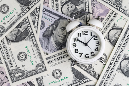 White alarm clock on US dollar banknotes as time for money awareness or compound interest of...