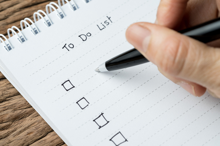To do lists, finish work, tasks priority concept, closed up of hand holding pen writing list on...