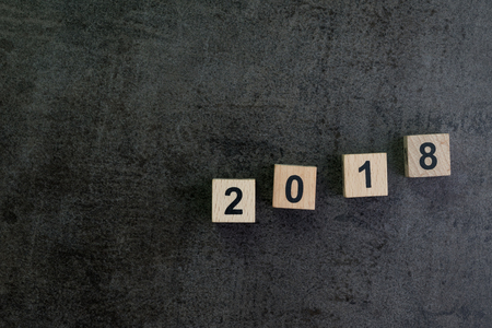 Year 2018 background or story ahead concept with wooden cube block number 2018 on dark black cement texture wallpaper background.の写真素材