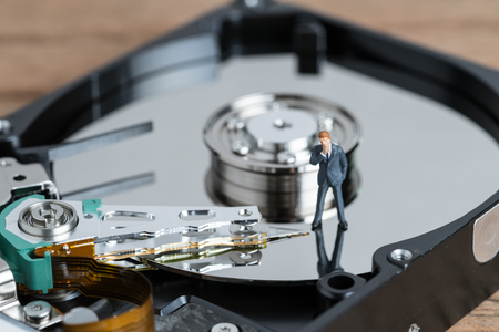 Digital IT business copy right, security or big data concept with miniature businessman thinking and standing beside read and write arm of hard disc drive platter.の写真素材