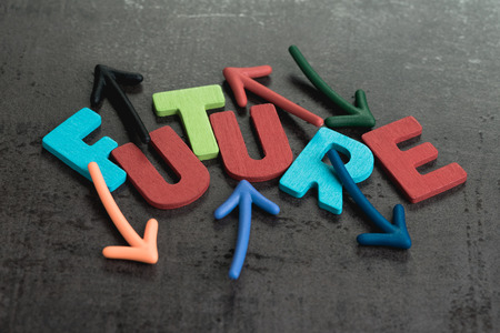 Wooden alphabets arrage word FUTURE with multi directional magnetic arrow on dark black chalckboard wall, risk or fear for life journey, uncertain future awareness.の写真素材