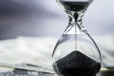 Closed up of sand falling in sandglass or hourglass on US Dollar bills as time running, long term...