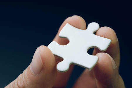 Discover solution or strategy missing piece for business success concept, hand holding a bright white paper jigsaw puzzle piece with dark black background.の写真素材