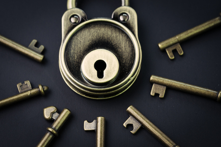 Security or secret protection concept, vintage brass padlock surrounded by multiple keys on a dark...