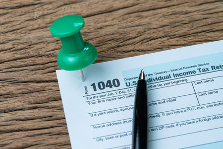 Big green thumbtack pin on 1040 individual income tax form with pen to fill in, reminder for yearly...