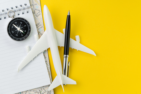 Flat lay or top view of black pen, miniature airplane, compass, notepad and map on vivid yellow background table with blank copy space, tourist, vacation or travel destination plan concept.の写真素材